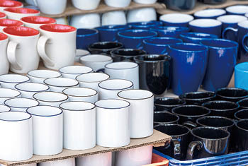 Focus on foreground of many various ceramic mugs display for sale at outdoor market