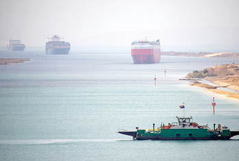 Suez Canal zone  Ship convoy in the distant desert haze  A local ferry between the east and west bank in foreground 